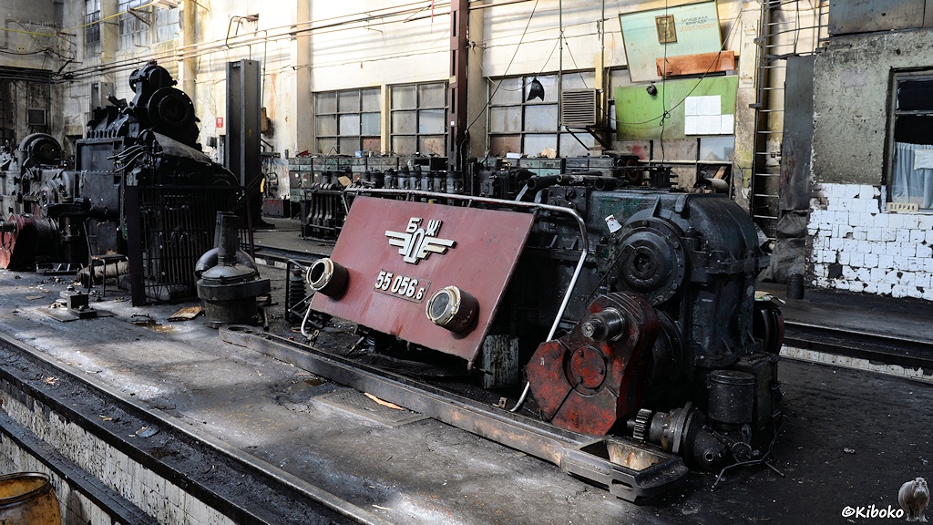 Das Bild zeigt die Frontklappe einer roten Diesellok angelehnt an einem Hydraulikgetriebe. Ein Motorblock steht weiter hinten in der Werkhalle.