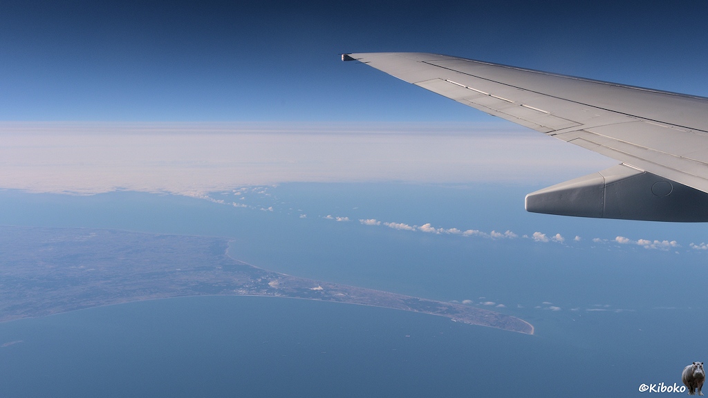 Das Bild zeigt eine Luftaufnahme einer langen schmalen Landzunge die weit ins blaue Meer hereinragt. Am linken Bildrand ragt die Tragfläche des Fliegers ins Bild.