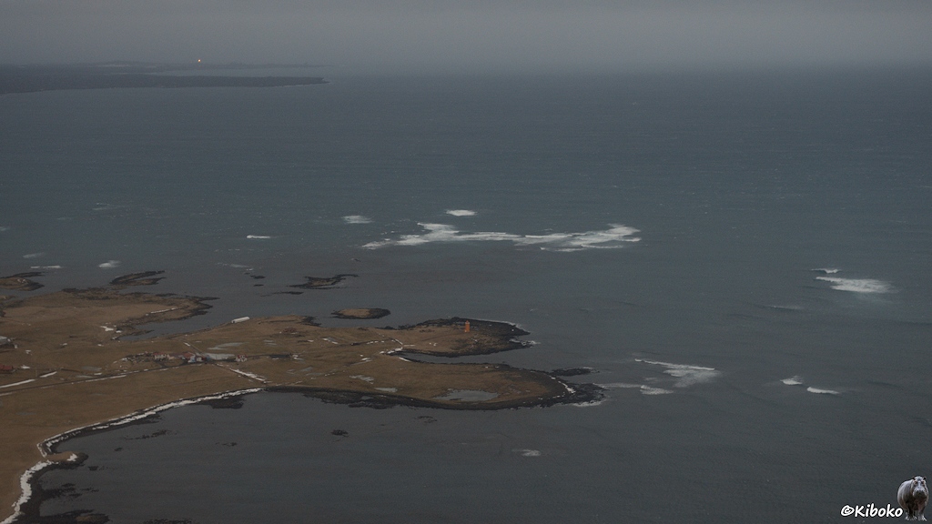 Luftaufnahme einer Halbinsel mit Doppelspitze im blaugrauen Meer. Die Wellen brechen sich im Meer. Auf einer Spitze steht ein oranger Leuchtturm.