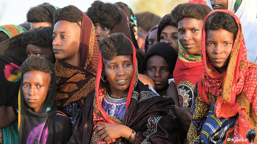 Das Bild zeigt die Porträts einer Gruppe Frauen mit bunten Kopftüchern. Unter den Kopftüchern schaut eine dichte, gelockte Haartracht hervor. Nur wenige Frauen schauen in die Kamera.
