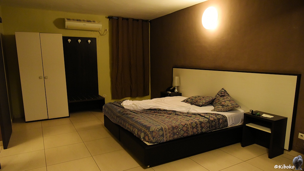 Das Bild zeigt ein Hotelzimmer mit Doppelbett, weißen Schrank, dunkelbrauner Wand und hellen Fliesen.