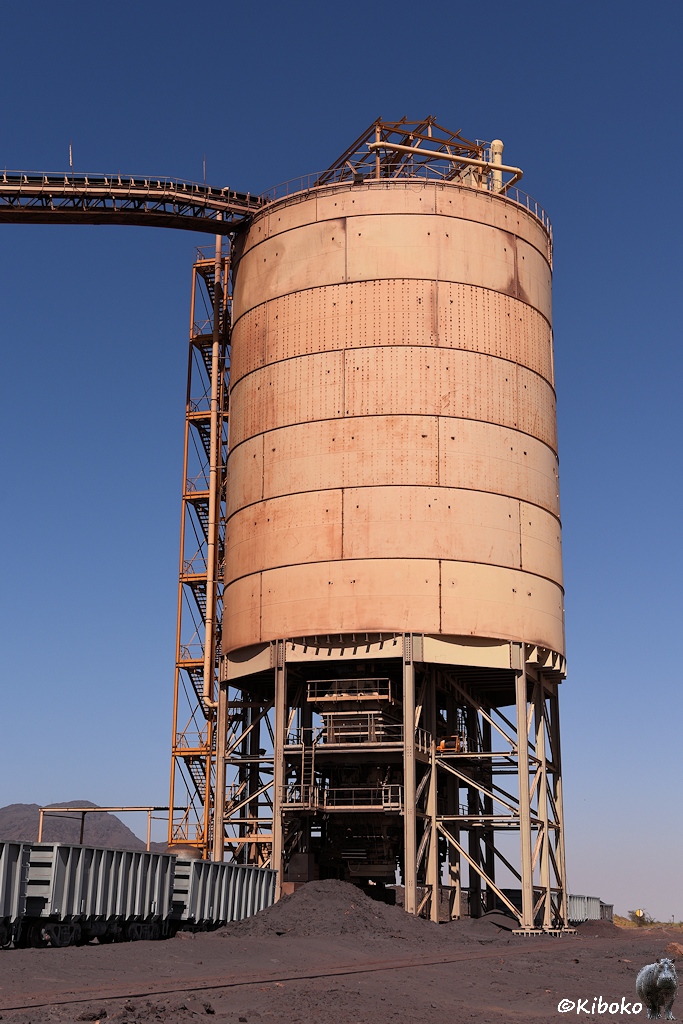 Ein großer, gelber, tonnenförmiger Silo steht auf Stahlstützen über einem Gleis.