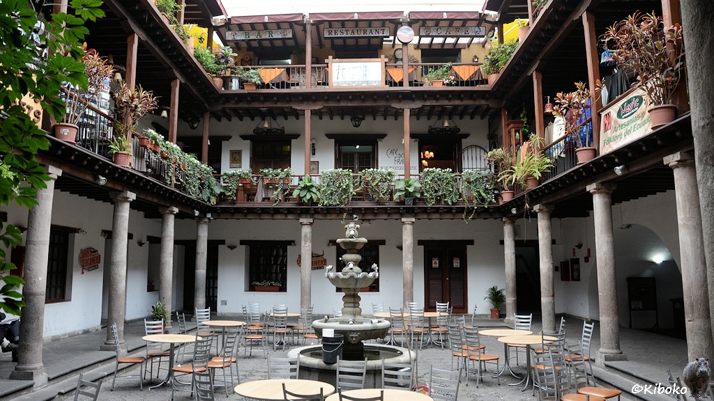 Das Bild zeigt den Innenhof eines dreistöckigen Gebäudes. In jeder Etage ist ein Säulengang, der zum Innenhof offen ist. Im Zentrum steht ein runder Steinbrunnen mit vier Becken übereinander.