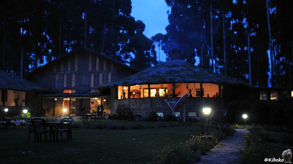 Das Bild zeigt nochmal das Hauptgebäude bei späterer Dämmerung. Die Beleuchtung aus der Rezeption und dem Restaurantgebäude hebt sich deutlich ab. Im Hintergrund zeichnen sich hohe Bäume gegen den Himmel zur blauen Stunde ab.