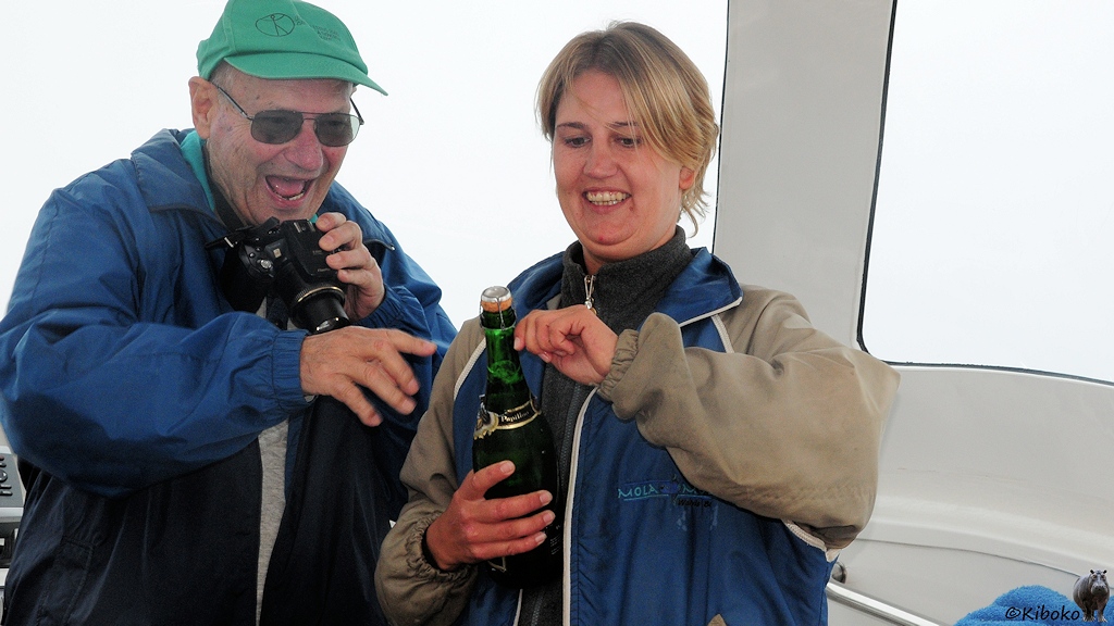Eine Frau öffnet eine Sektflasche. Der Tourist daneben kann es kaum erwarten.