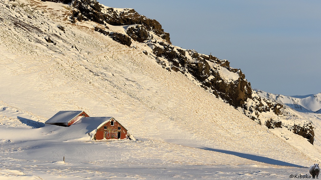 Das Bild zeigt ein rotbraunes, aufgelassenes Gehöft aus zwei Gebäuden. Der Schnee reicht an den Seiten bis zum Dach. Nur die Giebel schauen heraus. Die Fenster rund Türen fehlen.