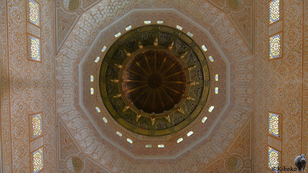 Das Bild zeigt den senkrechten Blick nach oben in die verzierte Kuppel. Die runde Kuppel ist ein 16 Sektoren unterteilt. Die Kuppel wird durch ein Zwölfeck mit 24 Fenstern getragen. Die Außenkannten des Zwölfecks gehen dann in ein Viereck über. Die Wände sind mit beigen Mosaiken verziert.