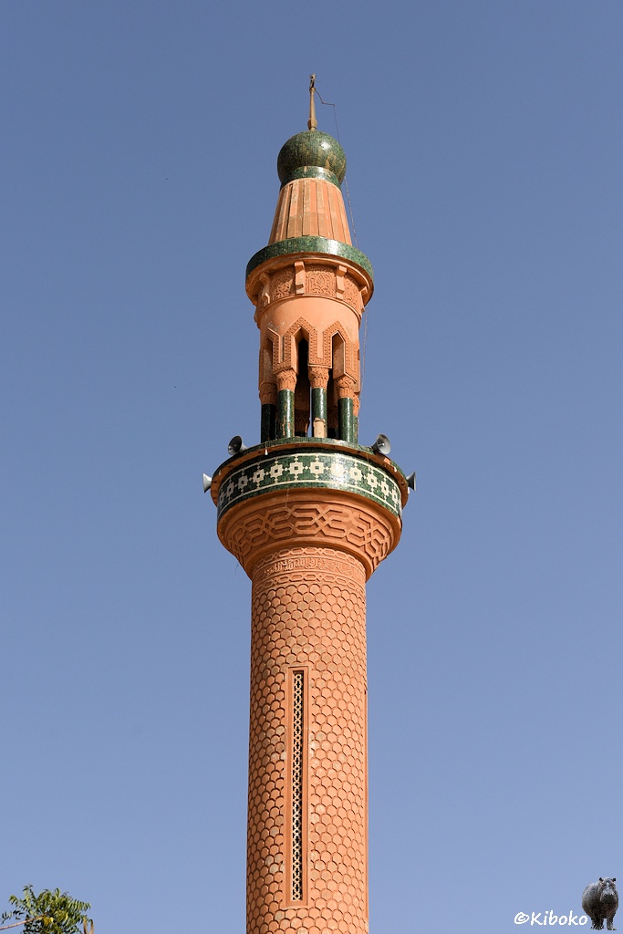 Das Bild zeigt eine Hochformataufnahme der Spitze vom Minarett. Ein Balkon hat ein grünes Mosaikmuster. Vier Lautsprecher stehen auf dem Balkon. Darüber steht die Spitze auf 8 Säulen. Konisch endet die Minarettspitze in einer grünen Kugel mit Blitzableiter.