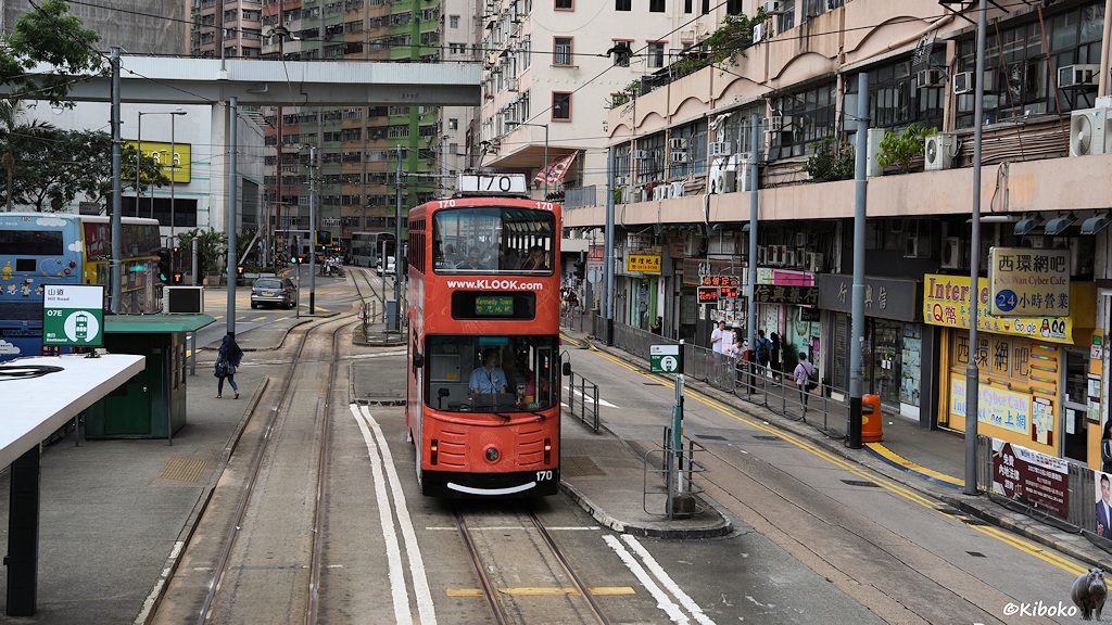 Das Bild zeigt die rote Doppelstrocktram 170 an einer Haltestelle auf einer Geschäftsstraße. Es ist eine modernisierte Tram mit großen Fenstern.