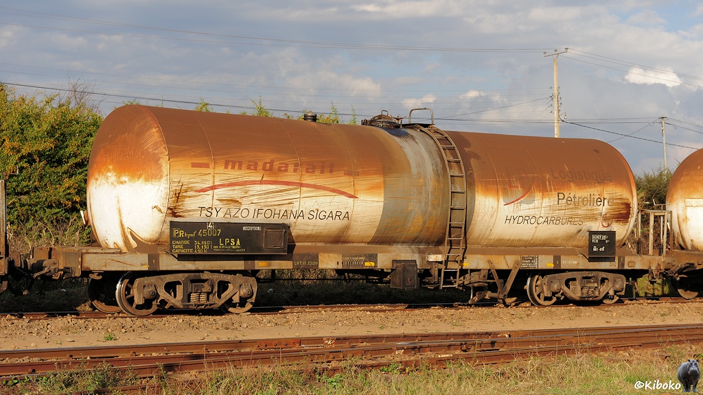 Ein weißer, vierachsiger Kesselwagen hat Speichenräder und ein graues Fahrwerk. Die obere Kesselhälfte ist rostbraun verdreckt. Der Kesselwagen hat die Aufschriften Madarail, Logistique Pétrolièr, Hydrocarbures und Tsy Azo Ifohana Sigara