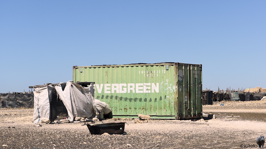Das Bild zeigt einen grünen Container, ein viereckigen Schuppen aus Stoffbahnen und eine Badewanne.