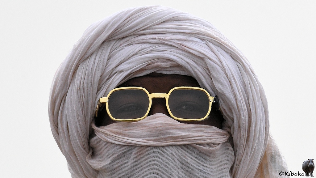 Das Bild zeigt das Porträt eines Mannes mit weißem Turban. Es bleibt nur ein Sehschlitz für die Augen, die mit einer Brille mit breitem Goldrahmen geschützt sind.