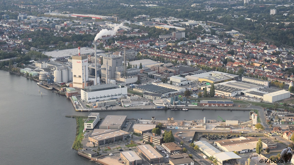 Das Bild zeigt ein Kraftwerk und einen kleinen Hafen an einem breiten Fluss.