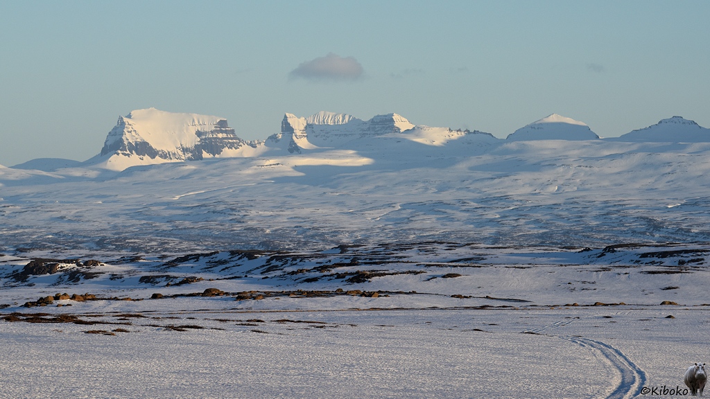 Hinter einen schneebedecken Tal ragen Berge mit hohen Felswänden empor.