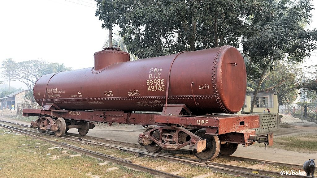 Das Bild zeigt einen braunen, vierachsigen Kesselwagen. Der Kessel ist mit Doppelreihen genietet. In der Mitte ist ein großer Dom. Zwei Spannbänder halten den Kessel auf dem Fahrwerk fest.