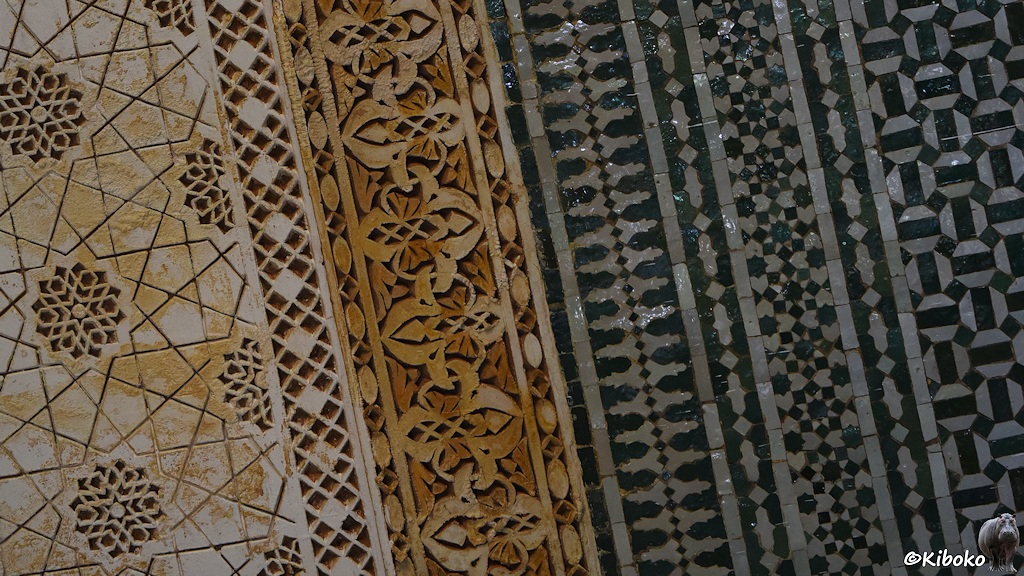 Das Bild zeigt mehrere utnerschiedliche Mosaiken und Steingravuren. Links sind zwei beige Mosaiken und Grafuren. Rechts sind grüne Mosaiken, die durch 5 senkrechte helle Linien unterteilt werden. Das Bild ist leich schräg gestellt.