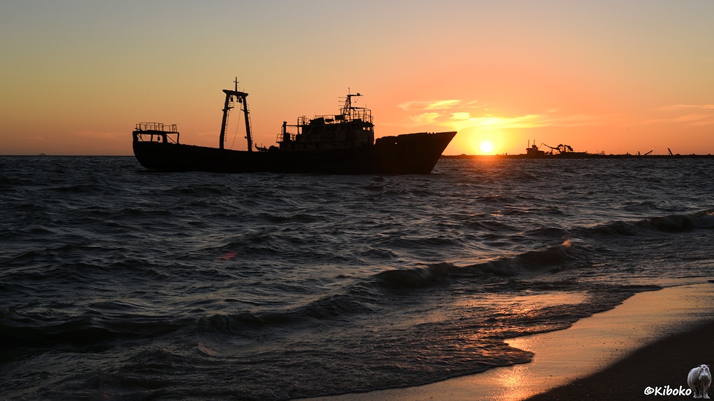 Das Bild zeigt die Silhouette eines Fischtrawlers gegen die vor dem Bug aufgehende Sonne vor gelborangem Himmel.