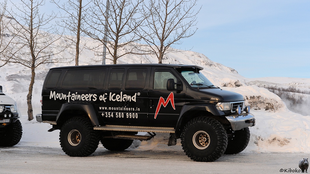 Das Bild zeigt einen hochgelegten Amerikanischen Kleinbus. Das Fahrzeug hat hohe, dicke Reifen mit viel Profil und Spikes. Es ist schwarz lackiert und hat die Aufschrift Mountaineers of Iceland