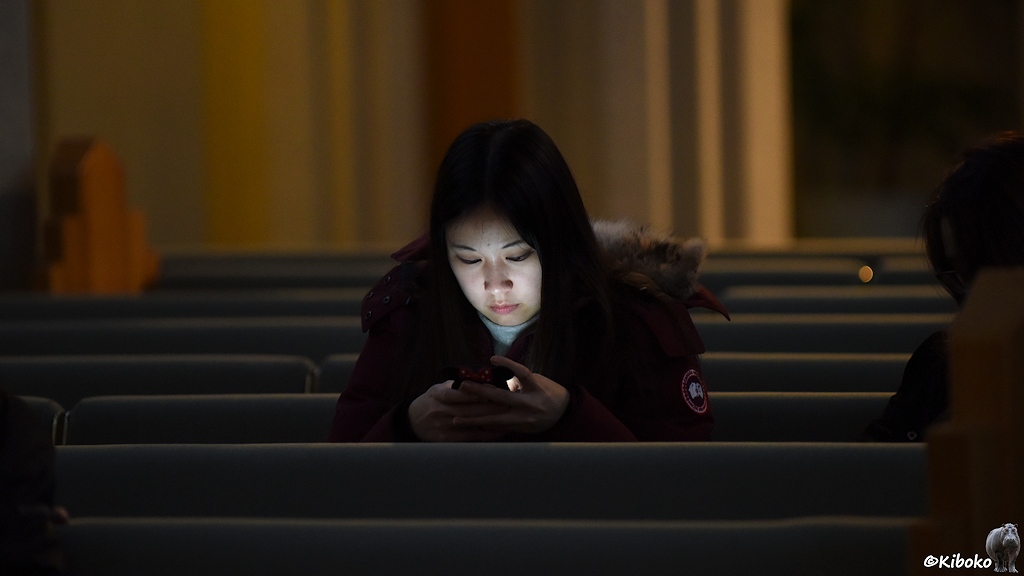 Eine junge frau sitzt auf einer Kirchbank und hat ihr Smartphone in den Händen. Das helle Gesicht wird vom Smartphone angestrahlt.