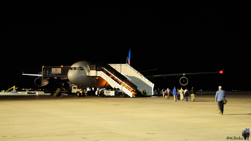 Im dunkeln steht ein vierstrahliger Flieger der Air Namibia auf dem Rollfeld. Passagiere laufen zum Flugzeug.