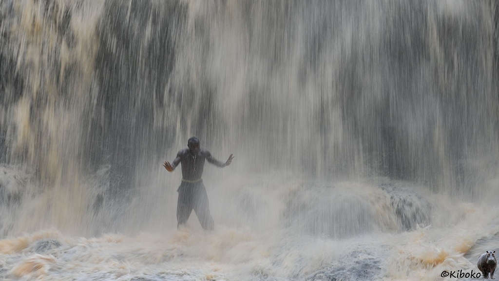 Einr Mann steht mitten im Wasserfall. Durch die lange Belichtungszeit fängt das Wasser an zu fließen.
