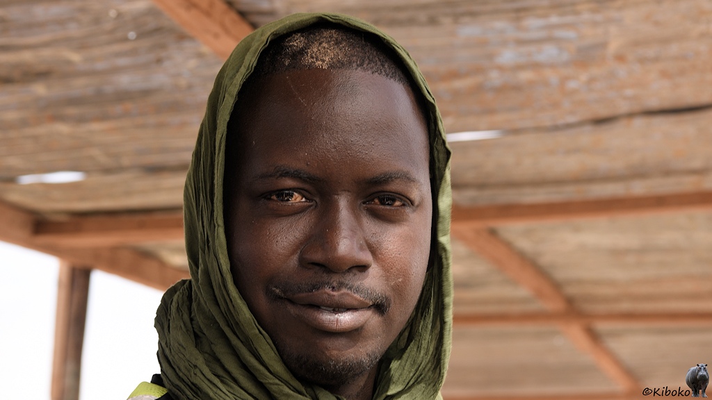 Das Bild zeigt das Porträt eines jungen Arbeiters aus Westafrika. Er trägt ein grünes Tuch zum Schutz gegen die Sonne.