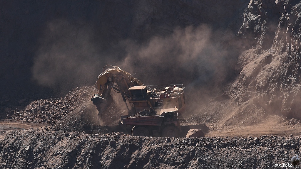 Der Bagger dreht sich weg. Der LKW hat bereits einen großen Erzhaufen auf der Ladefläche.