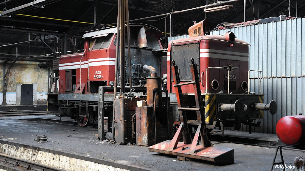 Das Bild zeigt eine rote Diesellokomoitve mit Mittelführerstand in eine Werkhalle. Die Klappen am Vorbau sind abmontiert. Der Motor fehlt.