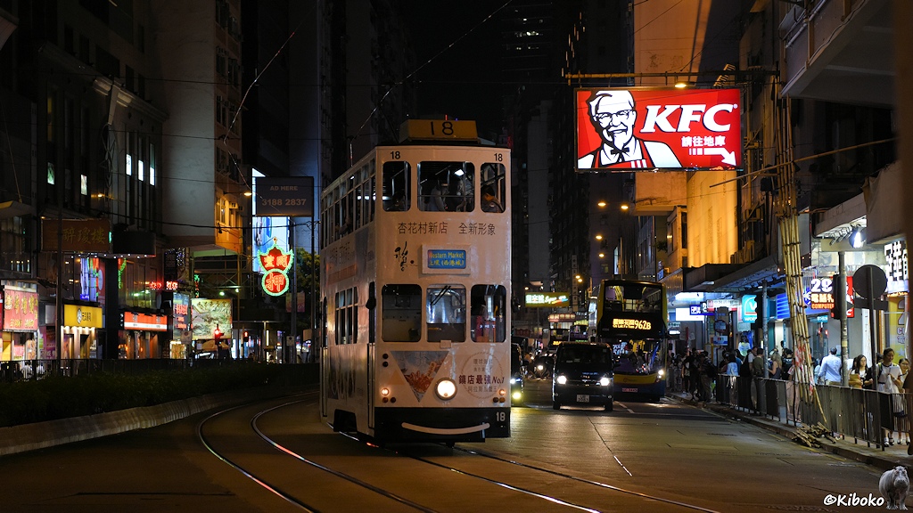 Das Bild zeigt die weiße Tram 18 beim überqueren einer Straße. Im Hintergrund ist die große rote Leuchtreklame mit den Buchstaben KFC.
