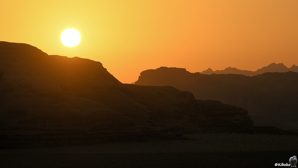 Sonne im orangefarbenen Himmel vor schwarzen Felsen.