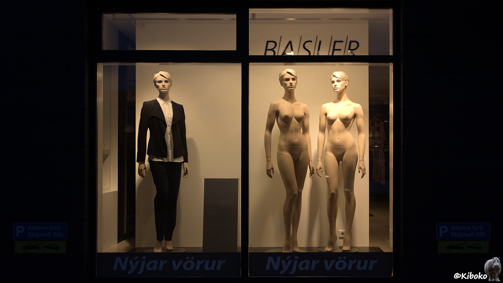 Ein einem Schaufenster stehen drei Schaufensterpuppe. Die linke Schaufensterpuppe trägt ein weiße Bluse, schwarze Jacke und schwarze Hose. Die rechten beiden Schaufensterpuppen sind nackt.