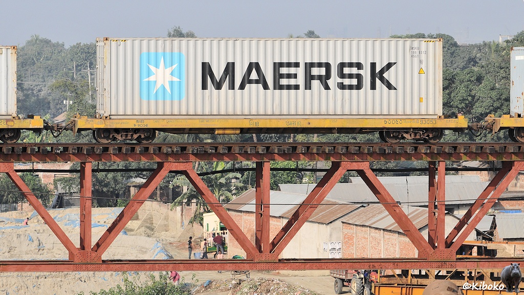 Das Bild zeigt einen gelben vierachsigen Containertragwagen in einem Containerzug auf einer Untergurtträgerbrücke. Der Wagen transportiert einen silbergrauen 40-Fuß-Container mit der schwarzen Aufschrift: MAERSK.