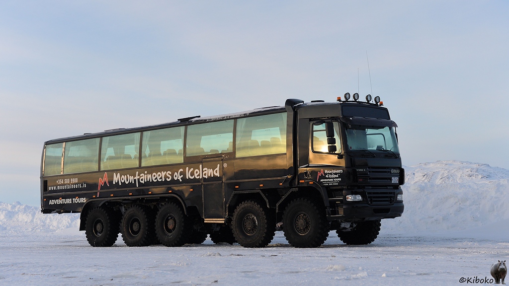 Das Bild zeigt einen schwarzen, fünfachsigen LKW mit Busaufbau. Der LKW hat große Räder mit dickem Profil. An der Seite steht die Aufschrift Mountainieers of Iceland und Adventure Tours.