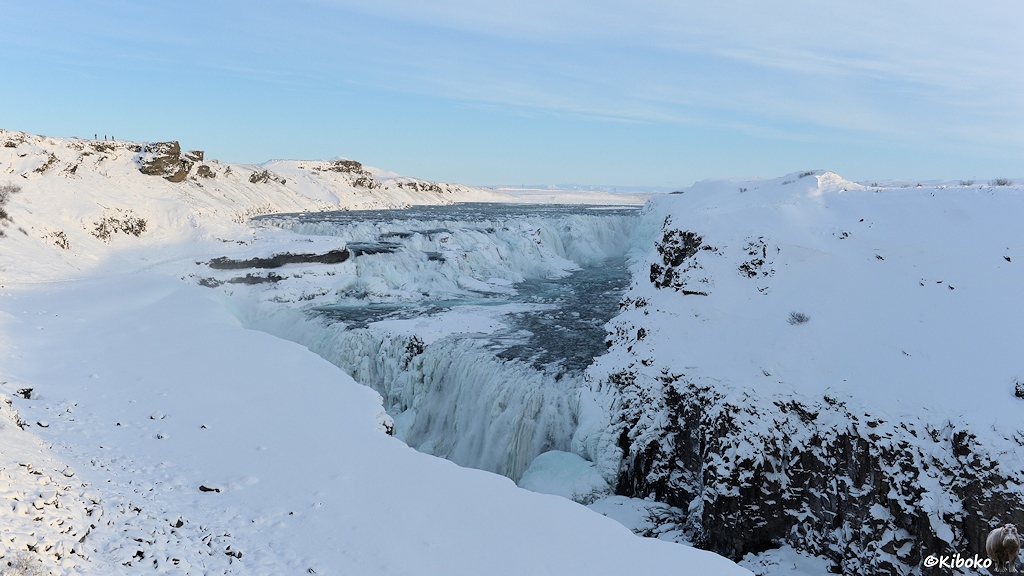 Das Bild zeigt den Wasserfall mit beiden Stufen in einer schneebedeckten Landschaft. Die beiden Stufen bilden einen 90° Winkel. Bei der oberen Stufe ist die linke Seite vorn. Bei der unteren Stufe ist die linke Seite hinten. Die linken Enden der beiden Stufen sind fast übereinander. Die untere Stufe stürzt in eine Schlucht. Eine schneebedeckte Abbruchkante im Vordergrund verhindert den Blick tief in die Schlucht.