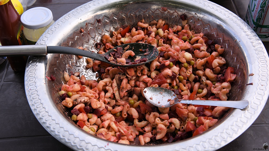 Das Bild zeigt eine Silberne Schüssel. Darin sind Nueln mit tomaten Erbsen und Rote Bete zusammengerührt. Zwei Löffel liegen auf den Nudeln.