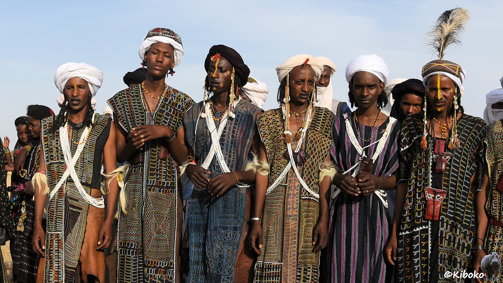 Das Bild zeigt sechs Männer in traditioneller dunkler Kleidung mit grünem Mustern und Turbanen. Fast alle tragen einen gelben Streifen von Stirn bis Nasenspitze.
