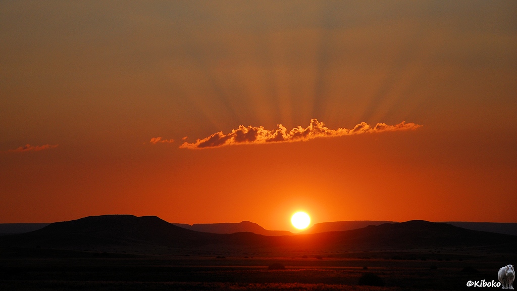 Die aufgehende Sonne taucht das Tal in orangenes Licht. Der Himmel leuchtet ornage. Ein paar Wolken erzeugen Sonnstrahlen am Himmel.