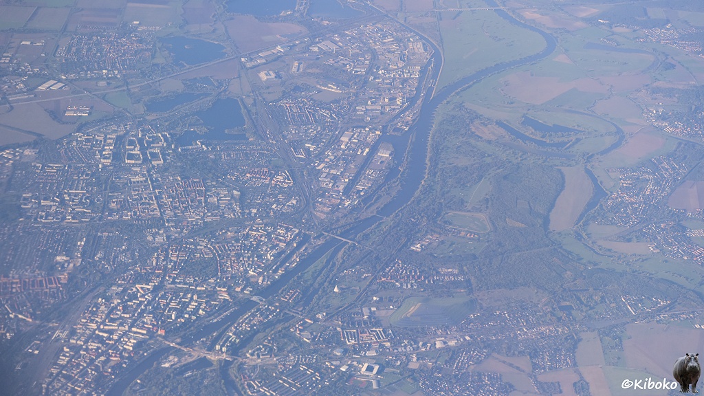 Das Bild zeigt eine Luftaufnahme aus großer Höhe einer Stadt die von einem breiten Fluss geteilt wird.