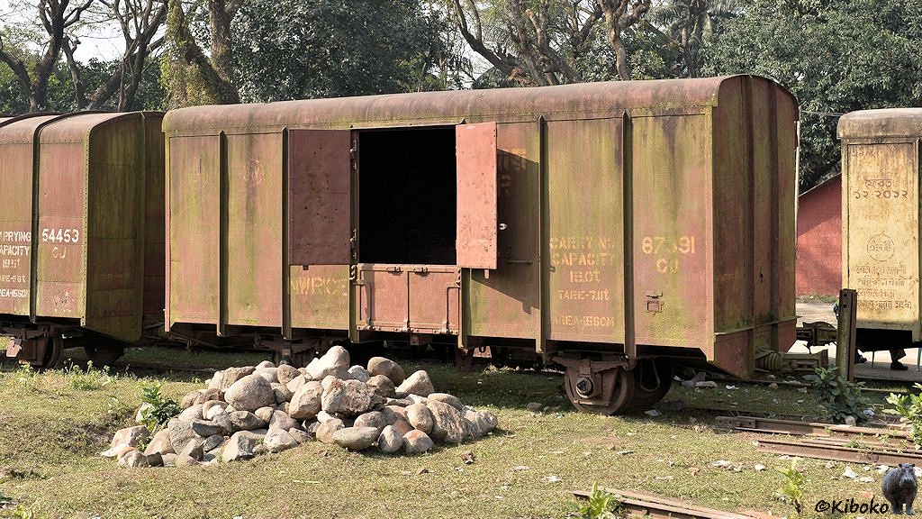 Das Bild zeigt einen braunen zweiachsigen gedeckten Güterwagen mit offenen Türflügeln. Der Wagen ist stark verweitter und mit grünem Moos überzogen. Die Lagerdeckel an den Achsen fehlen. Vor dem Wagen liegt ein Haufe großer heller abgerundeter Steine.