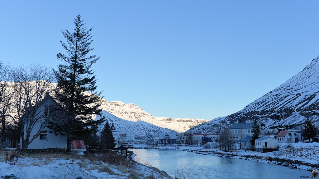 Holzhäuser stehen am Zufluss zum Fjord in einer Winterlandschaft.