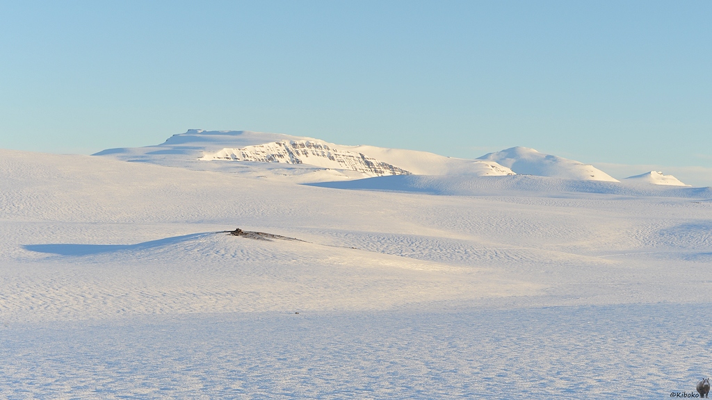 Sanfte Hügel sind mit Schnee bedeckt. Im Hintergrund sind schneebedeckte Felswände.