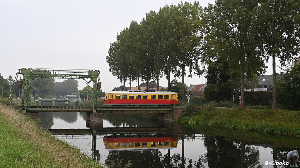 Das Bild zeigt einen rot-beigen Triebwagen auf einer Klappbrücke. Der Triebwagen spiegelt sich im darunterliegenden Fluß