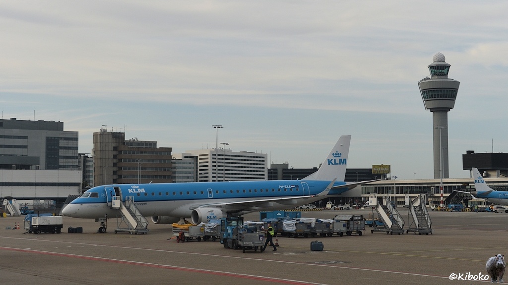 Das Bild zeigt ein kleinen blauen Düsenflüeger vor einem Terminal und einen Kontrollturm auf einem Flughafen.