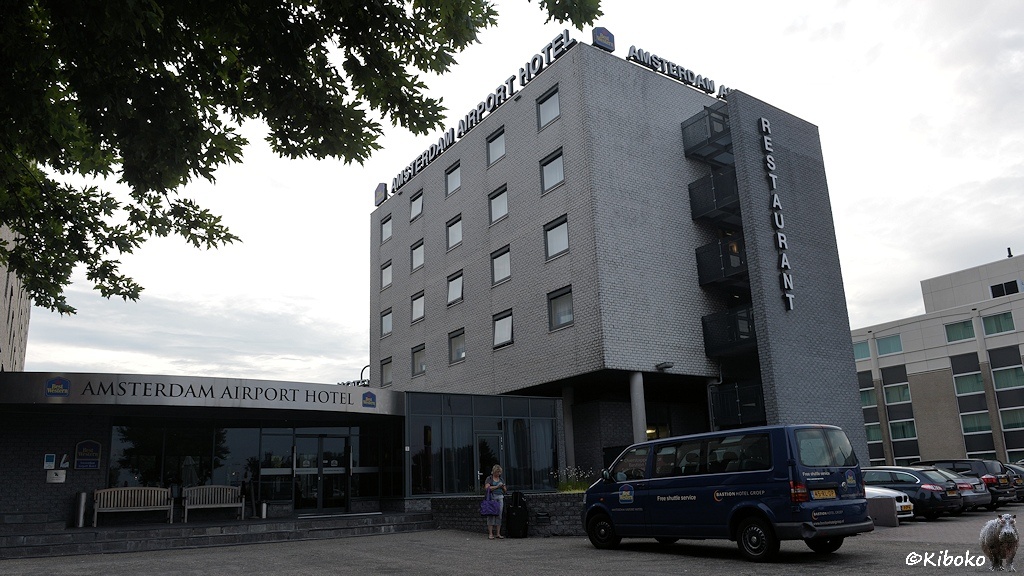 Das Bild zeigt ein fünfstöckiges, würfelförmiges mit einem flachen Anbau. Daran steht: Amsterdam Airport Hotel.