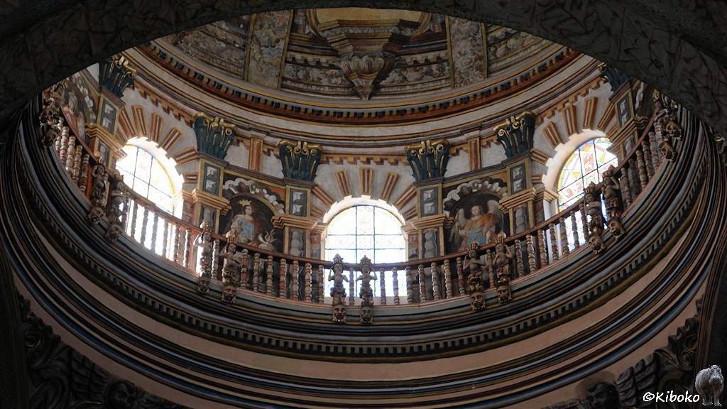 Das Bild zeigt einen schrägen Blick nach oben in die Kuppel. Die runde Kuppel ist innen von einer Balustrade umgeben. Zwischen den Fenstern sind Figuren und sehr viel Zierrat.
