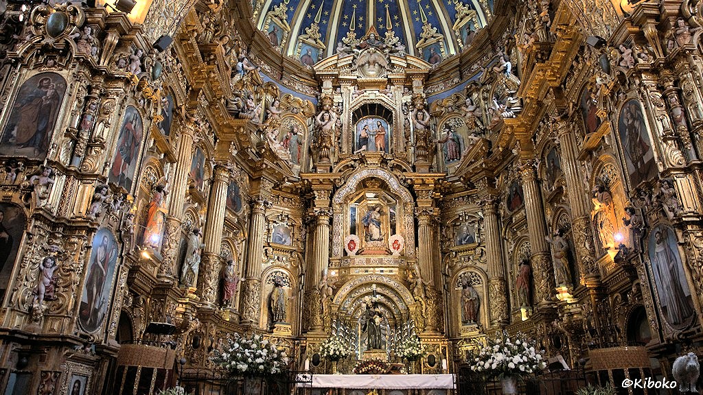 Das Bild zeigt den Altarraum aus der Nähe. Der Hochaltar ist durch Säulen gegliedert. Dazwischen sind Gemälde und Figuren. Alles glänzt golden.