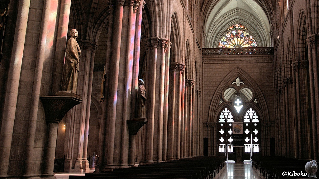 Das Bild zeigt einen Innenansicht der Kirche zurück zu den LIchtdurchfluteten Eingangspforte mti spitzebögen. Hohe Säulen tragen das hohe Dach. An jeder Säule ist eine überlebensgroße Figur.