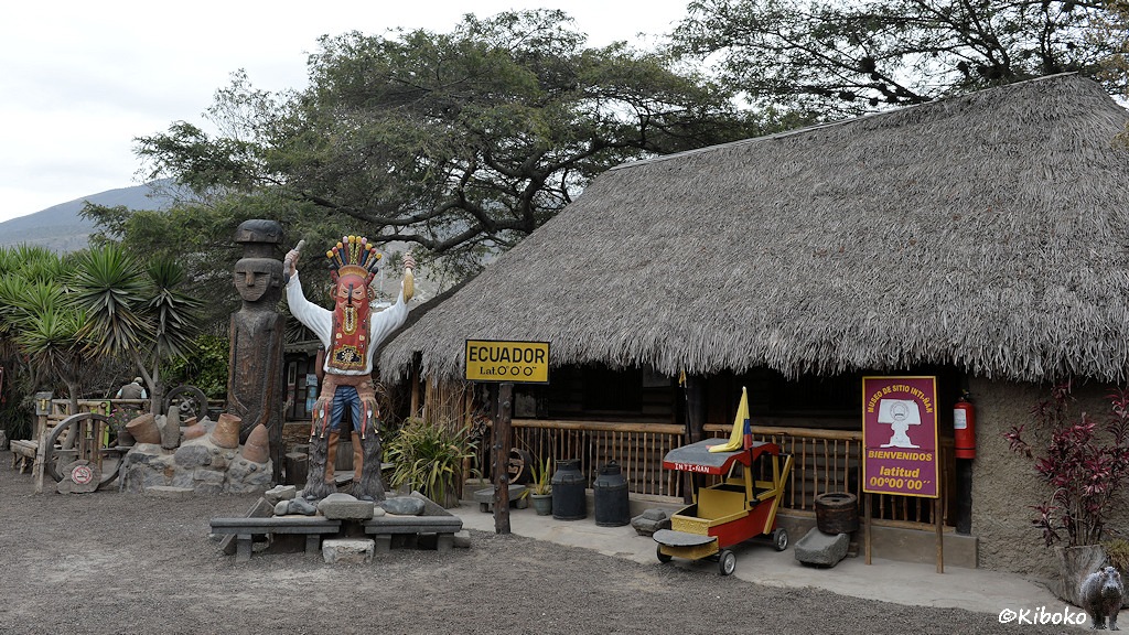 Das Bild zeigt den Eingangsbereich mit einer großen Strohgedeckten Hütte, einen überlebensgroße Indianerstatue und einem gelben Schild mit der schwarzen Schrift: ECUADOR.
