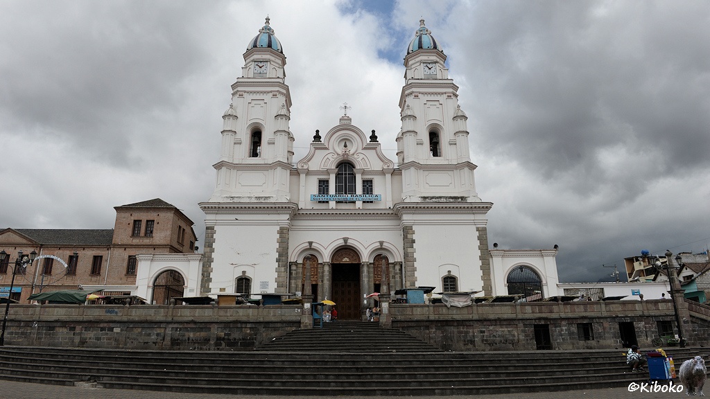 Das Bild zeigt das Portal einer weißen Kirche mit zwei Türmen. Die Türme haben gestreifte Kuppeln in hellblau und dunkelblau. Die Kirche steht auf einem erhöhten Podest, welches durch eine breite Treppe erreicht wird.