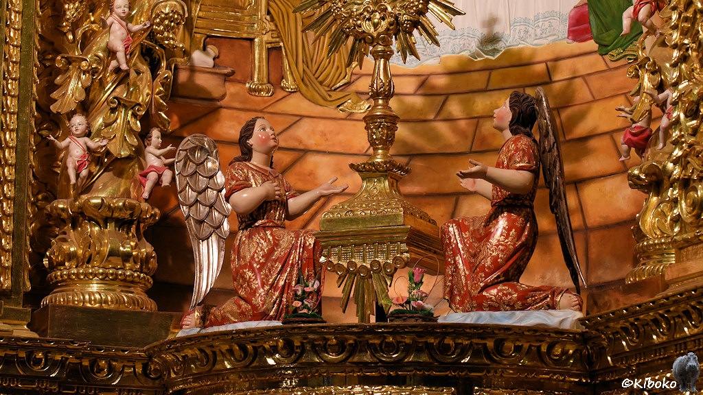 Das Bild zeigt zwei gegenüberknienenden Engel im rot-goldenen Kleid mit ausgebreiteten Armen. Die Wangen sind rot gefärbt. Die Engel schauen auf einer reich verzierten goldenen Säule an der jeweils drei nackte Jünglinge mit roten Pampas hängen.